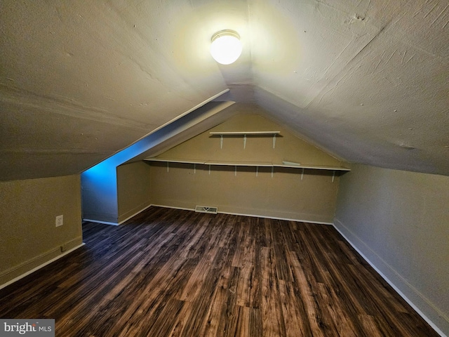 additional living space with a textured ceiling, dark wood-type flooring, and lofted ceiling