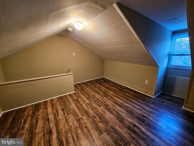 additional living space with dark hardwood / wood-style flooring, lofted ceiling, and a textured ceiling