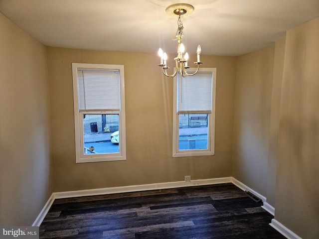 spare room with dark hardwood / wood-style flooring, plenty of natural light, and an inviting chandelier