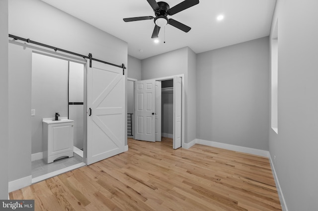 unfurnished bedroom with a barn door, ceiling fan, and light hardwood / wood-style floors