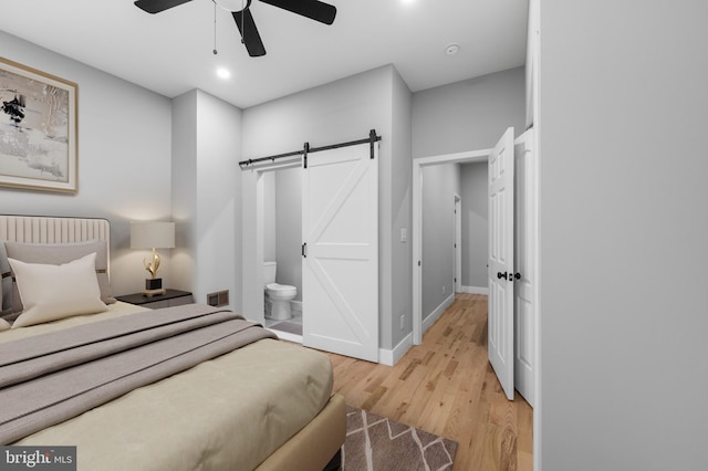 bedroom with ceiling fan, a barn door, light wood-type flooring, and connected bathroom