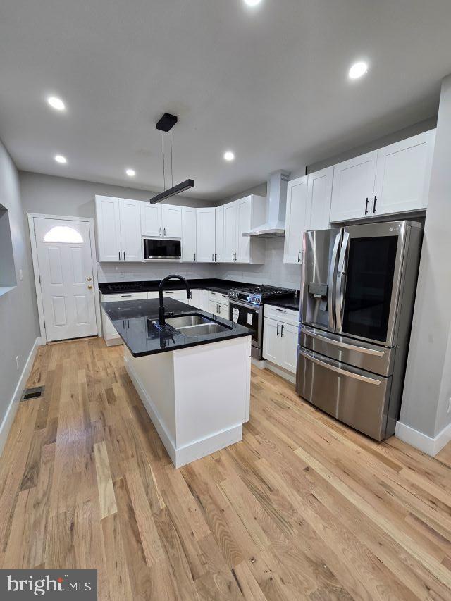 kitchen with white cabinetry, wall chimney exhaust hood, decorative light fixtures, and appliances with stainless steel finishes