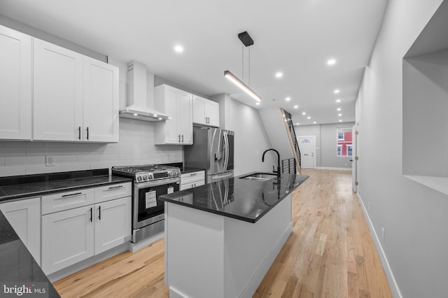 kitchen featuring light wood-type flooring, stainless steel appliances, sink, wall chimney range hood, and hanging light fixtures