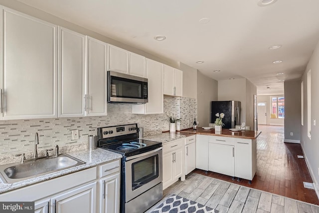 kitchen with kitchen peninsula, appliances with stainless steel finishes, light wood-type flooring, sink, and white cabinetry