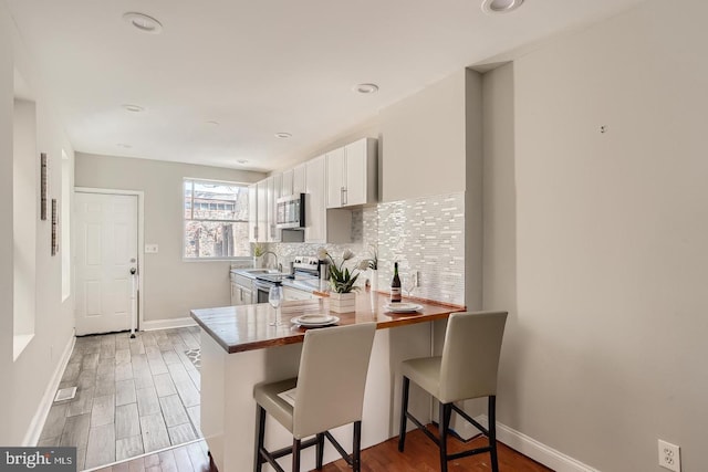 kitchen with stainless steel appliances, kitchen peninsula, a breakfast bar area, decorative backsplash, and white cabinets