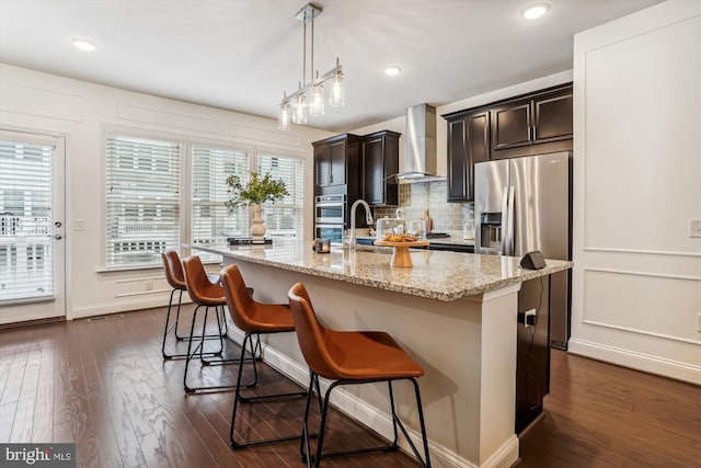 kitchen with a center island with sink, wall chimney exhaust hood, dark hardwood / wood-style floors, and a kitchen breakfast bar