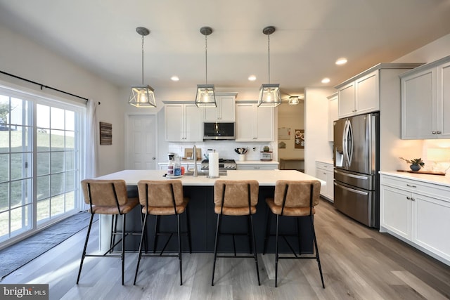 kitchen with pendant lighting, hardwood / wood-style flooring, a kitchen island with sink, and appliances with stainless steel finishes