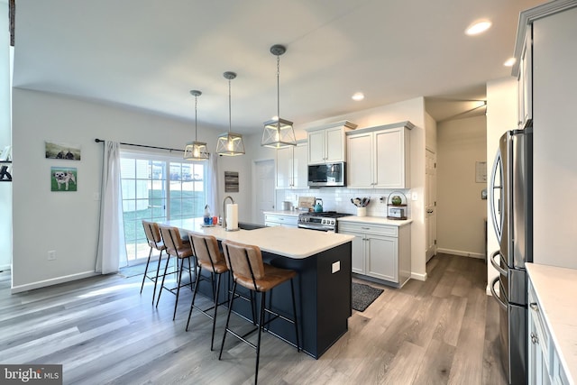 kitchen with appliances with stainless steel finishes, a center island with sink, decorative light fixtures, hardwood / wood-style floors, and a breakfast bar area