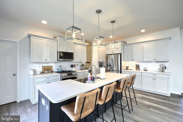 kitchen with appliances with stainless steel finishes, a kitchen island with sink, pendant lighting, wood-type flooring, and a breakfast bar area