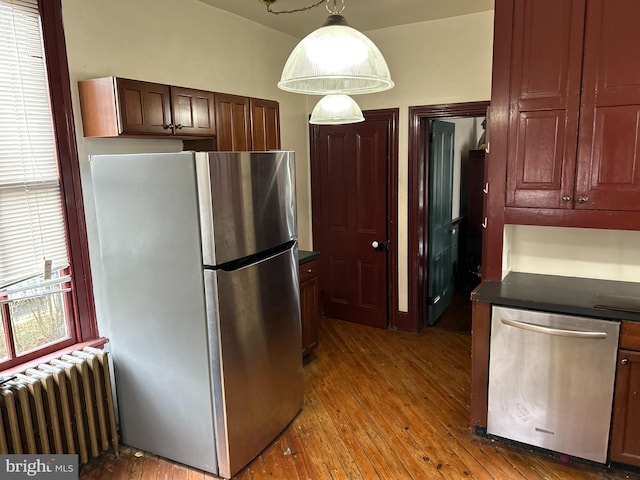 kitchen with appliances with stainless steel finishes, a wealth of natural light, hardwood / wood-style flooring, and radiator