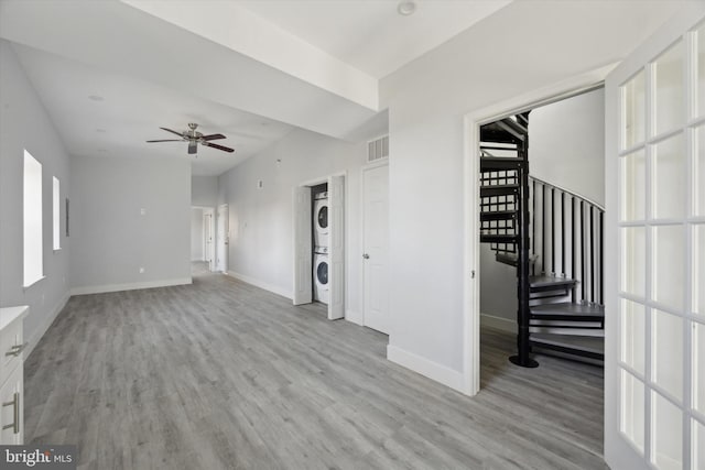 unfurnished living room with plenty of natural light, ceiling fan, light hardwood / wood-style flooring, and stacked washer and clothes dryer