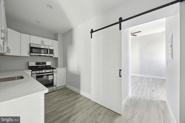 kitchen featuring light hardwood / wood-style floors, a barn door, white cabinetry, and appliances with stainless steel finishes