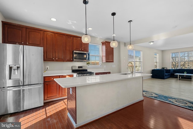 kitchen featuring appliances with stainless steel finishes, sink, decorative light fixtures, dark hardwood / wood-style floors, and an island with sink