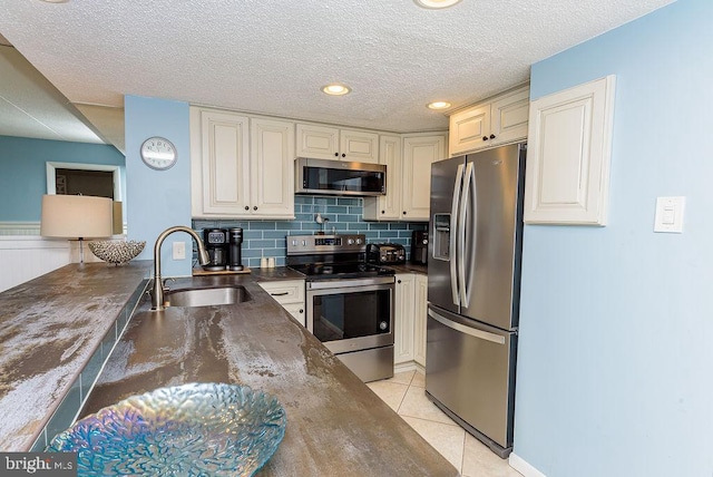 kitchen with sink, stainless steel appliances, tasteful backsplash, a textured ceiling, and light tile patterned floors