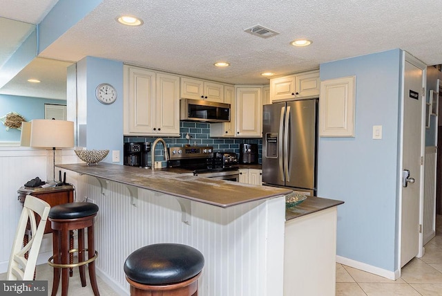 kitchen featuring kitchen peninsula, a kitchen breakfast bar, decorative backsplash, stainless steel appliances, and light tile patterned flooring