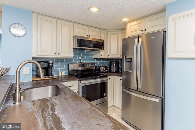 kitchen featuring sink, light tile patterned floors, a textured ceiling, appliances with stainless steel finishes, and tasteful backsplash