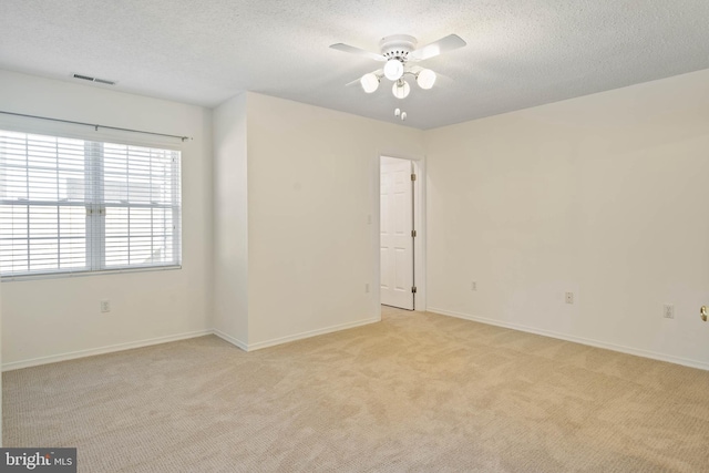 empty room featuring a textured ceiling, light colored carpet, and ceiling fan