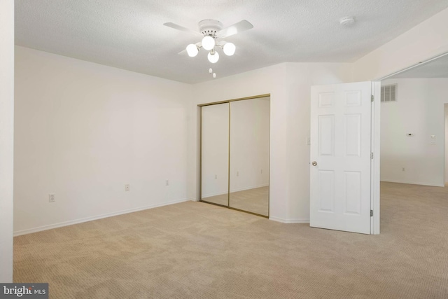 unfurnished bedroom with a textured ceiling, a closet, ceiling fan, and light colored carpet