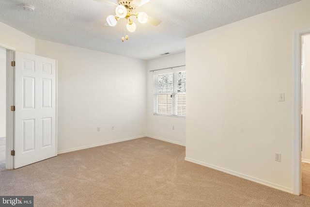 empty room with ceiling fan, light colored carpet, and a textured ceiling