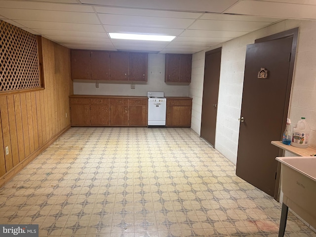 kitchen with white stove, a drop ceiling, and wooden walls