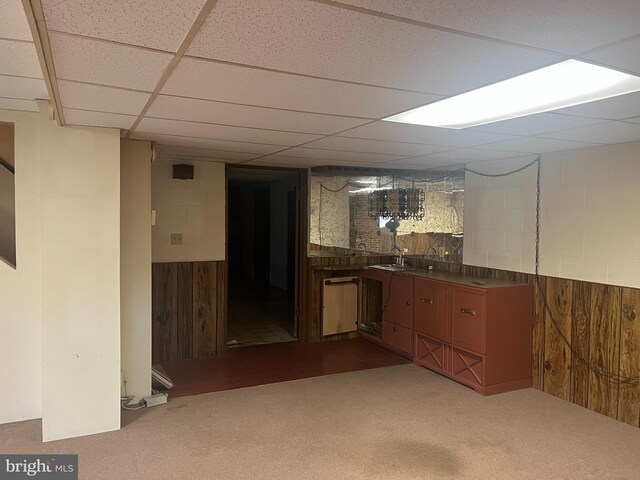 bar featuring a drop ceiling, dark carpet, sink, and wooden walls