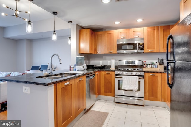 kitchen with kitchen peninsula, appliances with stainless steel finishes, sink, decorative light fixtures, and dark stone countertops