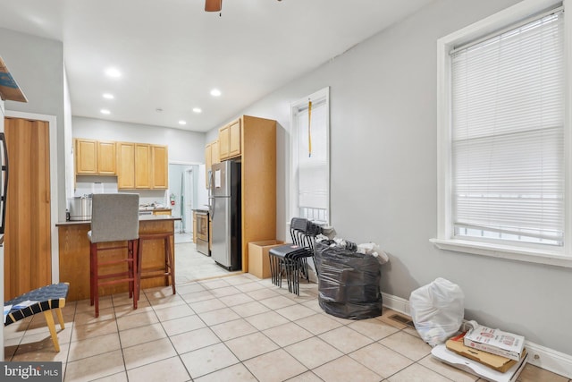 kitchen featuring a healthy amount of sunlight, stainless steel fridge, light brown cabinetry, and a breakfast bar area