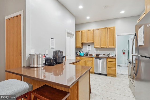 kitchen with a breakfast bar, light brown cabinetry, sink, light tile patterned floors, and stainless steel appliances