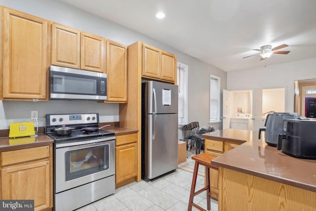 kitchen featuring light brown cabinets, light tile patterned floors, ceiling fan, stainless steel appliances, and washer / clothes dryer