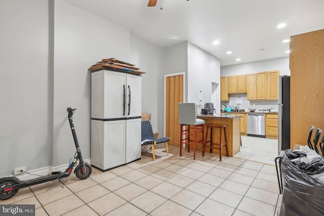 kitchen with a breakfast bar area, light tile patterned floors, light brown cabinets, appliances with stainless steel finishes, and ceiling fan