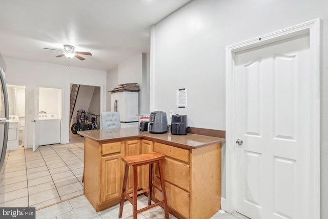 kitchen featuring washer / clothes dryer, light tile patterned floors, ceiling fan, kitchen peninsula, and light brown cabinets