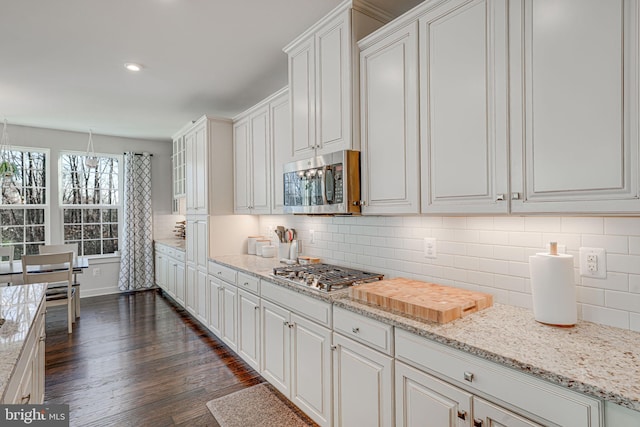 kitchen with light stone countertops, appliances with stainless steel finishes, tasteful backsplash, dark wood-type flooring, and white cabinets