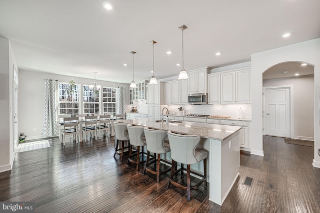 kitchen featuring white cabinetry, dark hardwood / wood-style flooring, pendant lighting, a center island with sink, and appliances with stainless steel finishes