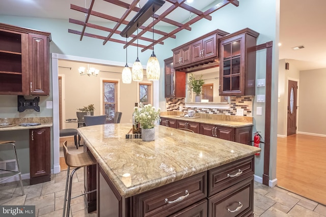 kitchen featuring an inviting chandelier, a kitchen breakfast bar, backsplash, pendant lighting, and a kitchen island