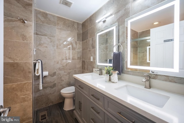 bathroom featuring vanity, toilet, a shower with shower door, and tile walls