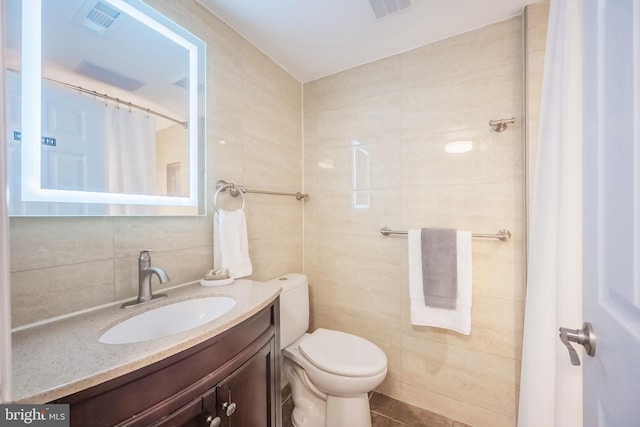 bathroom featuring tile patterned flooring, vanity, toilet, and tile walls