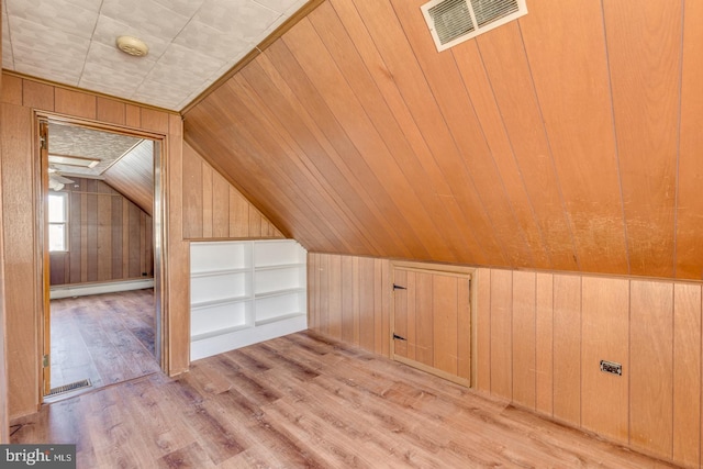 additional living space with baseboard heating, wood walls, light hardwood / wood-style flooring, and lofted ceiling