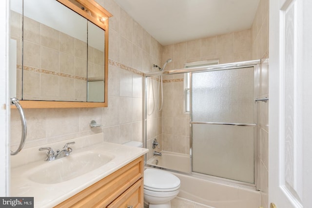 full bathroom featuring vanity, backsplash, bath / shower combo with glass door, toilet, and tile walls