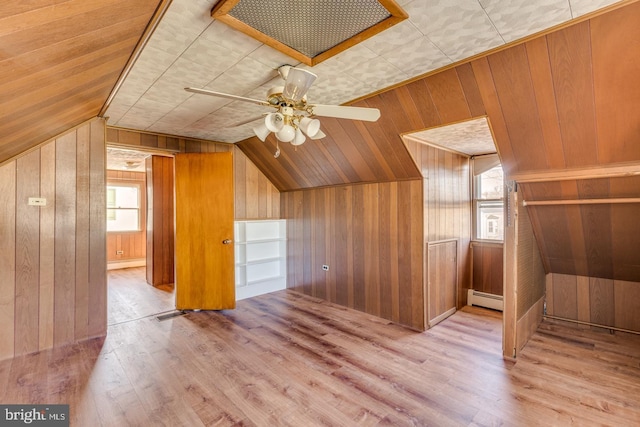 additional living space featuring light wood-type flooring, vaulted ceiling, ceiling fan, a baseboard radiator, and wood walls