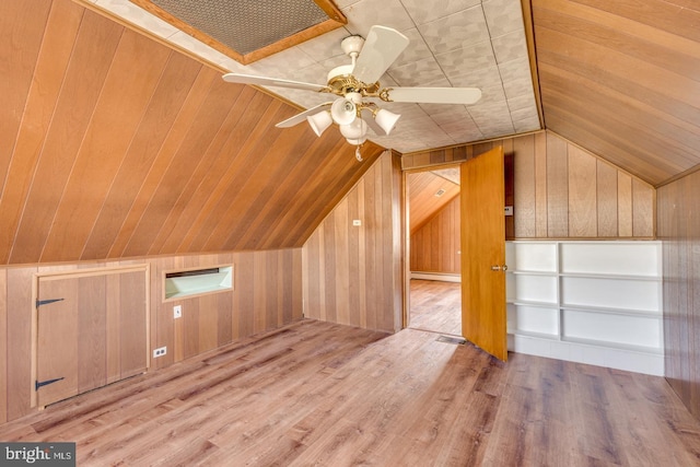 additional living space with wood walls, light hardwood / wood-style flooring, ceiling fan, and vaulted ceiling