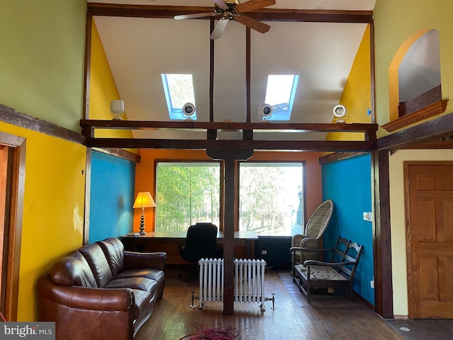 living room with dark wood-type flooring, high vaulted ceiling, radiator, a skylight, and ceiling fan