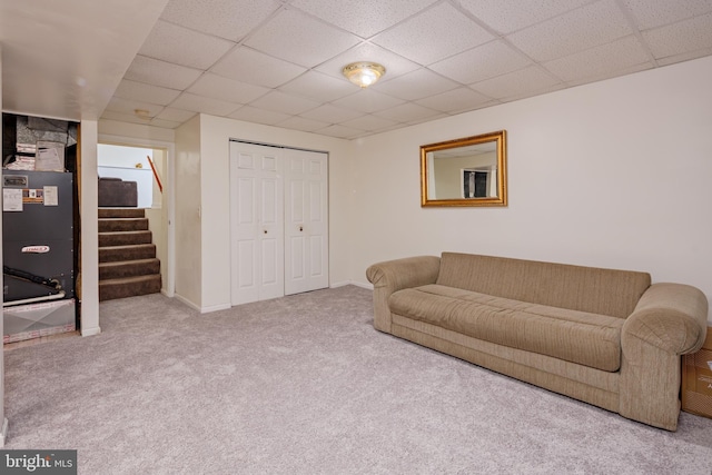 carpeted living room featuring heating unit and a drop ceiling