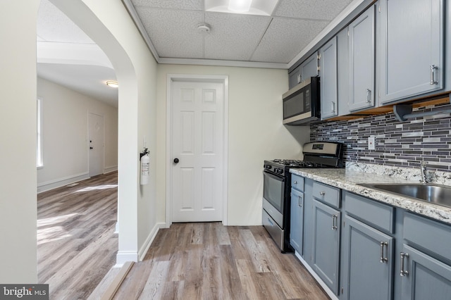 kitchen featuring a paneled ceiling, sink, light wood-type flooring, tasteful backsplash, and stainless steel appliances