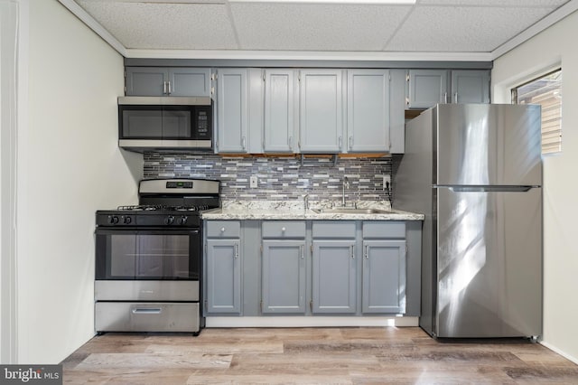 kitchen with a paneled ceiling, sink, stainless steel appliances, and light hardwood / wood-style flooring