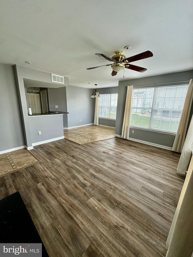 unfurnished living room with wood-type flooring and ceiling fan with notable chandelier