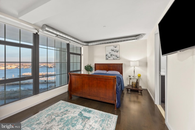 bedroom with dark hardwood / wood-style flooring and a water view