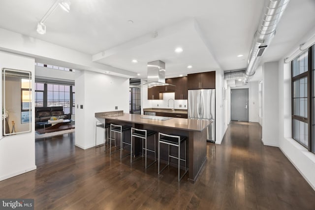 kitchen with dark hardwood / wood-style flooring, island exhaust hood, stainless steel fridge, a kitchen bar, and dark brown cabinets