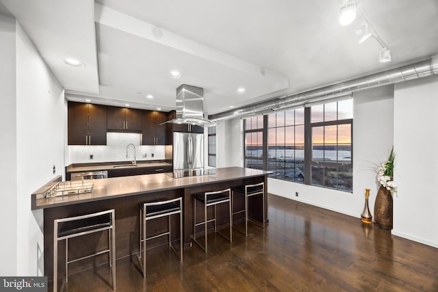 kitchen with stainless steel refrigerator, a kitchen breakfast bar, dark hardwood / wood-style flooring, island range hood, and dark brown cabinets