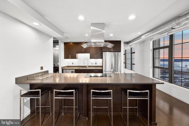 kitchen with dark wood-type flooring, island exhaust hood, kitchen peninsula, a breakfast bar, and appliances with stainless steel finishes