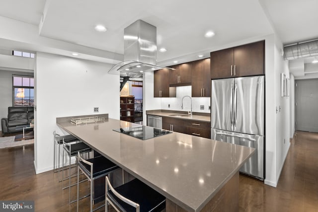 kitchen featuring appliances with stainless steel finishes, dark hardwood / wood-style flooring, a breakfast bar, island range hood, and sink